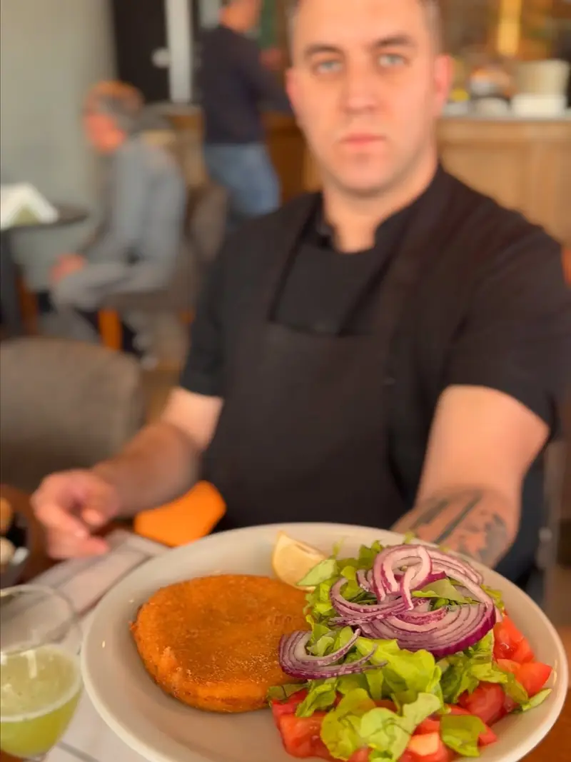 El cocinero con un plato de milanesa y ensalada